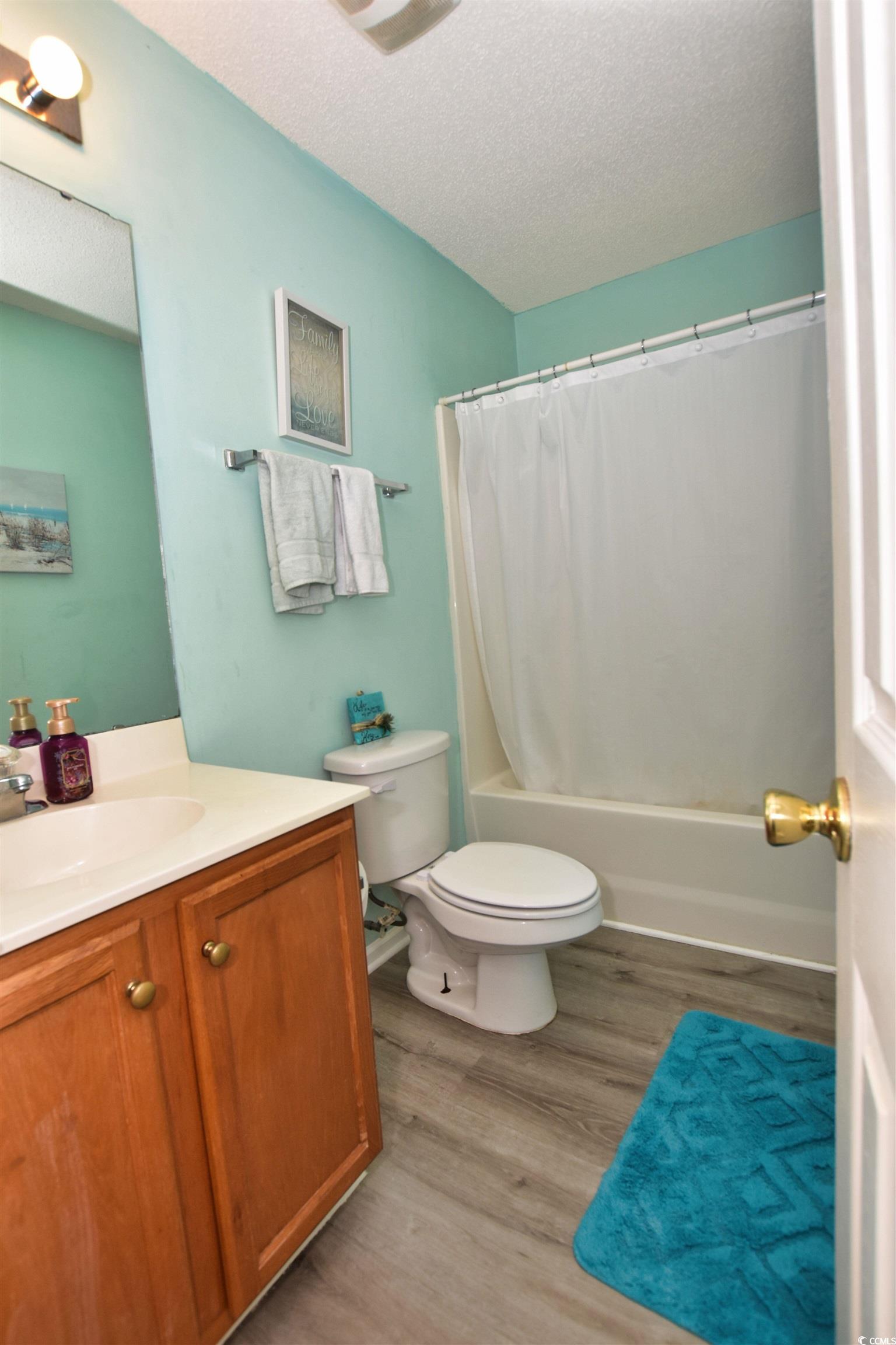 1065 Pinwheel Loop, Unit 1065 Myrtle Beach, SC 29577 - Photo 17 of 27 Full bathroom featuring shower / bathtub combination with curtain, a textured ceiling, toilet, vanity, and wood-type flooring