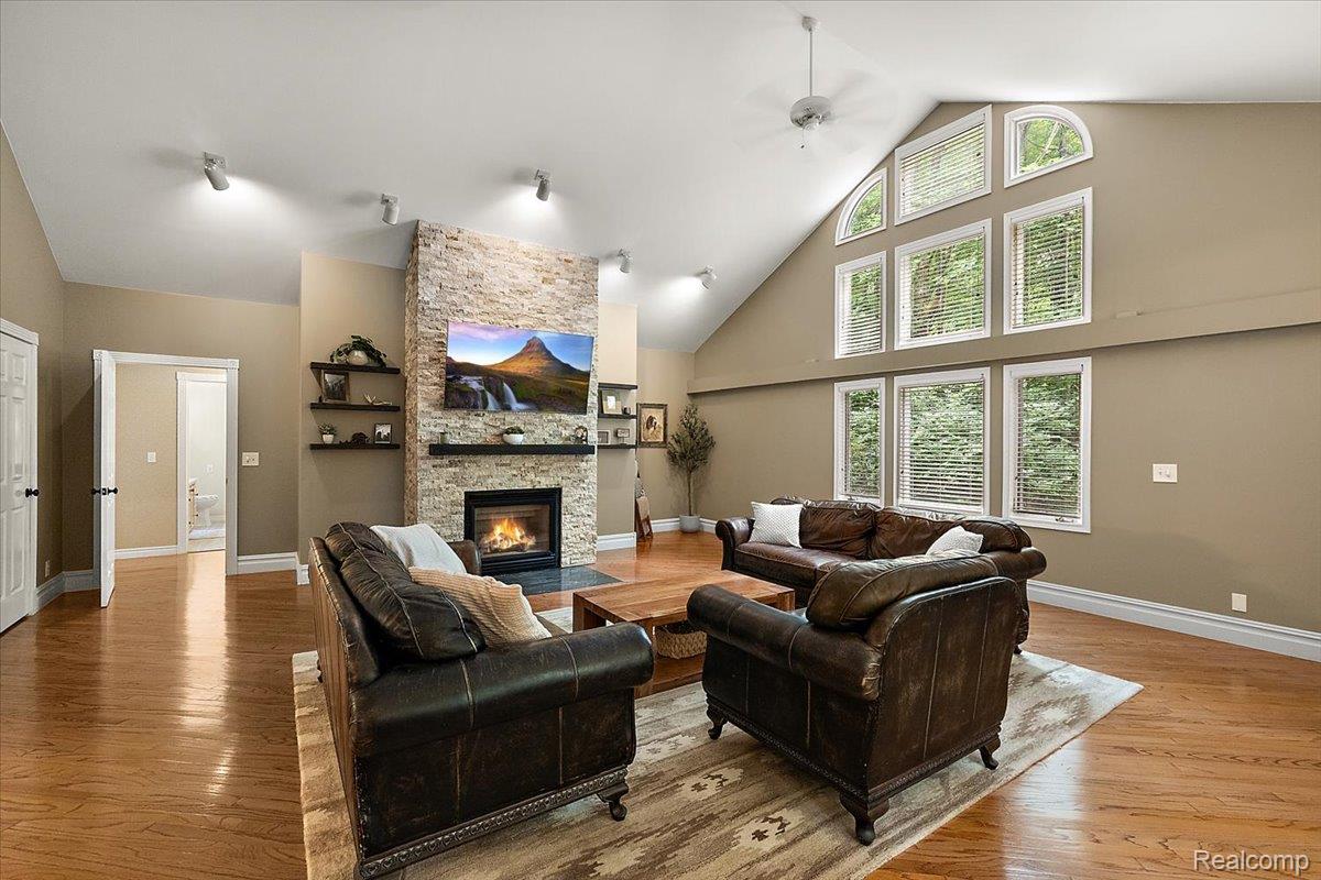 4219 Gardner Road Metamora, MI 48455 - Photo 14 of 84 Living area featuring a vaulted ceiling with a ceiling fan, a stone-clad fireplace, and multiple tall windows