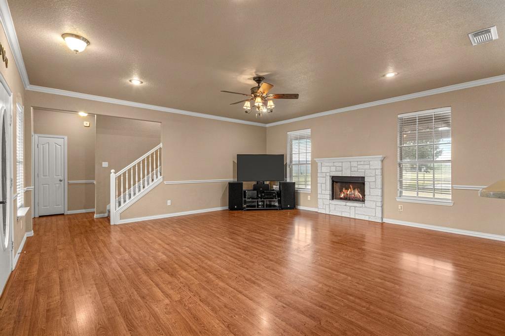 6501 Indian Trail Sanger, TX 76266 - Photo 4 of 39 Unfurnished living room with a textured ceiling, ceiling fan, a stone fireplace, crown molding, and wood finished floors