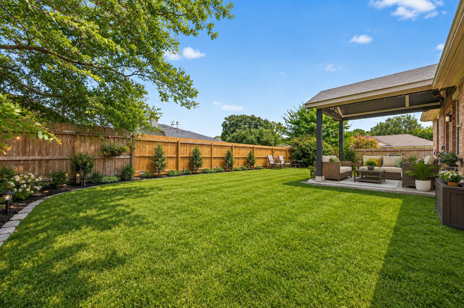 3418 Lockgate Drive Spring, TX 77388 - Photo 46 of 47 This oversized backyard is beautifully landscaped, featuring a manicured lawn bordered by neatly spaced shrubs and a stone-edged garden bed. The covered patio offers a comfortable seating area, while the full privacy fence and mature trees create a peaceful, park-like setting. This photo has been virtually staged or enhanced.