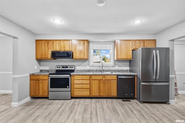 a kitchen with stainless steel appliances granite countertop a stove a sink dishwasher a refrigerator and a microwave oven with wooden floor