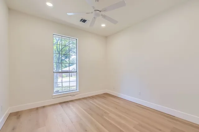 an empty room with wooden floor chandelier fan and windows