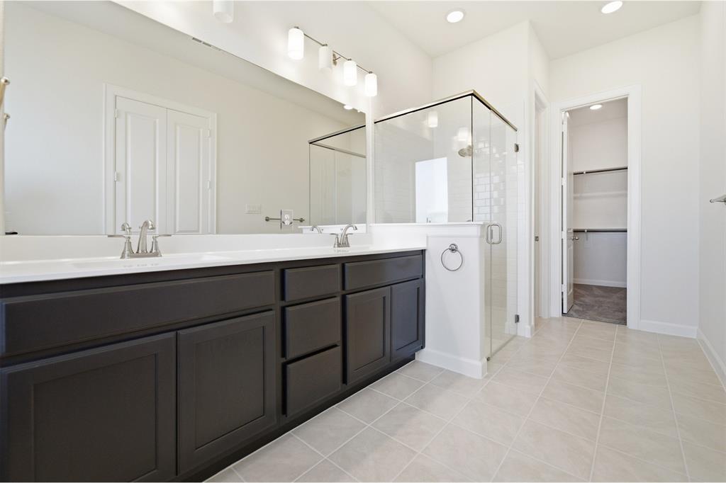 2020 Casting Ridge Mesquite, TX 75181 - Photo 22 of 34 Bathroom featuring a dual vanity with dark wood-finish cabinetry, a large frameless mirror, a glass-enclosed shower with subway tile, and light-toned floor tiling