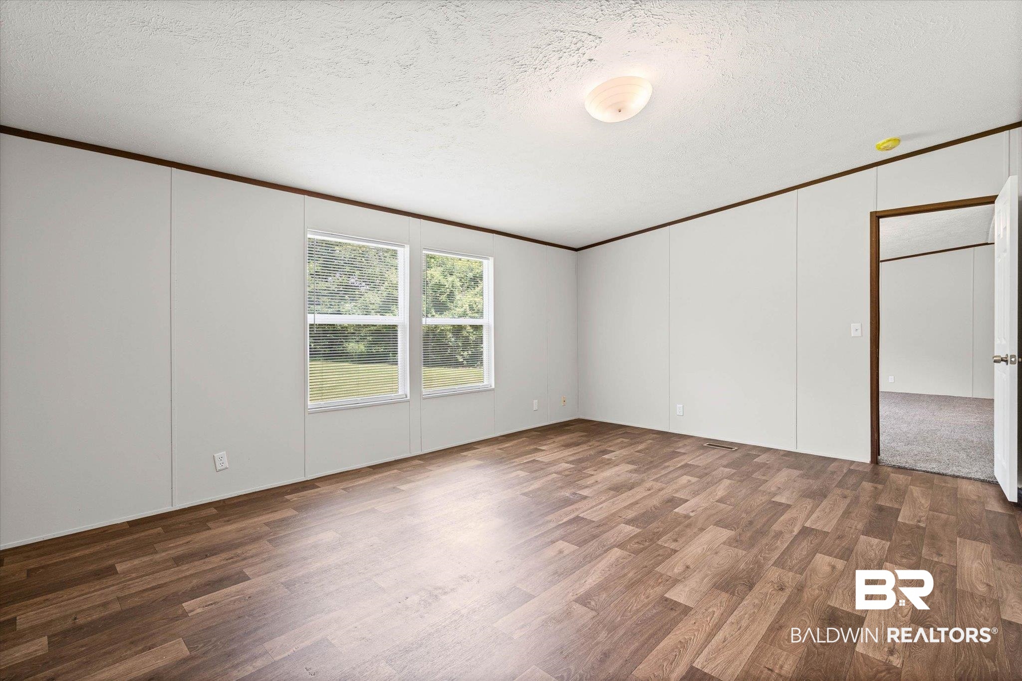 25366 Pollard Road Daphne, AL 36526 - Photo 13 of 22 Spacious room featuring wood-finish flooring, light-toned wall paneling, and two windows providing natural illumination