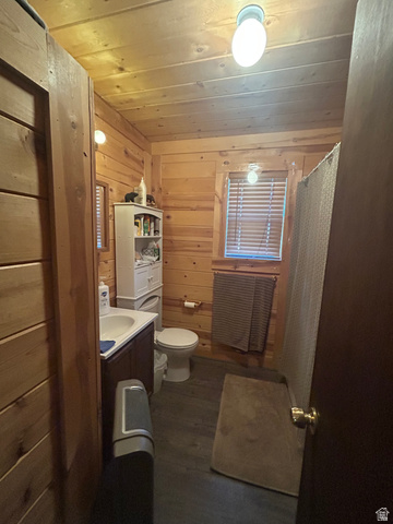 19075 West Honesty Cove Duchesne, UT 84021 - Photo 15 of 44 Wood-paneled bathroom featuring a dark wood vanity with an integrated sink, a toilet, a window with blinds, and wood-finish flooring