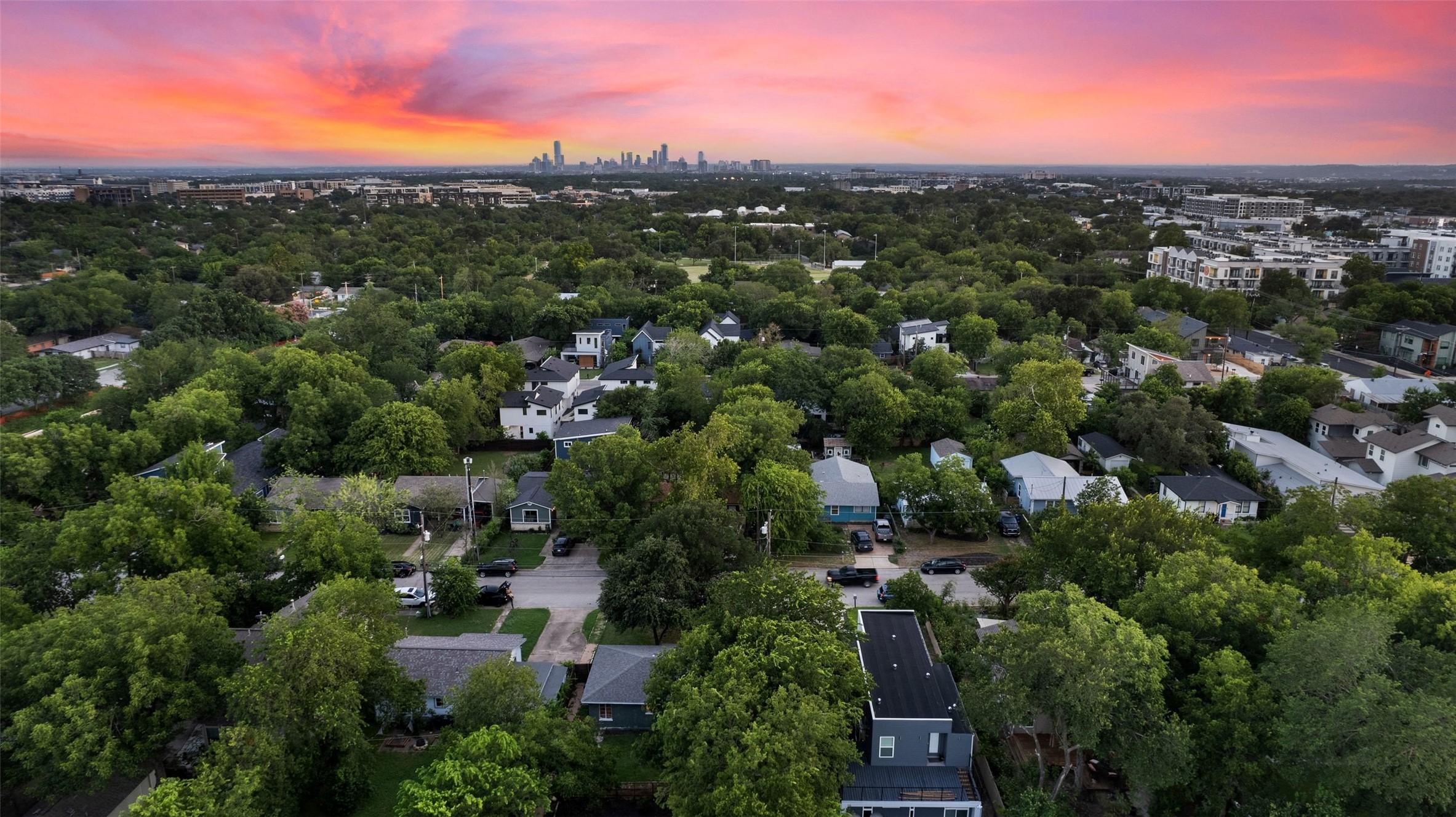 412 West Croslin Street Austin, TX 78752 - Photo 1 of 36 A vibrant sunset over a lush neighborhood, offering a glimpse of the distant city skyline.