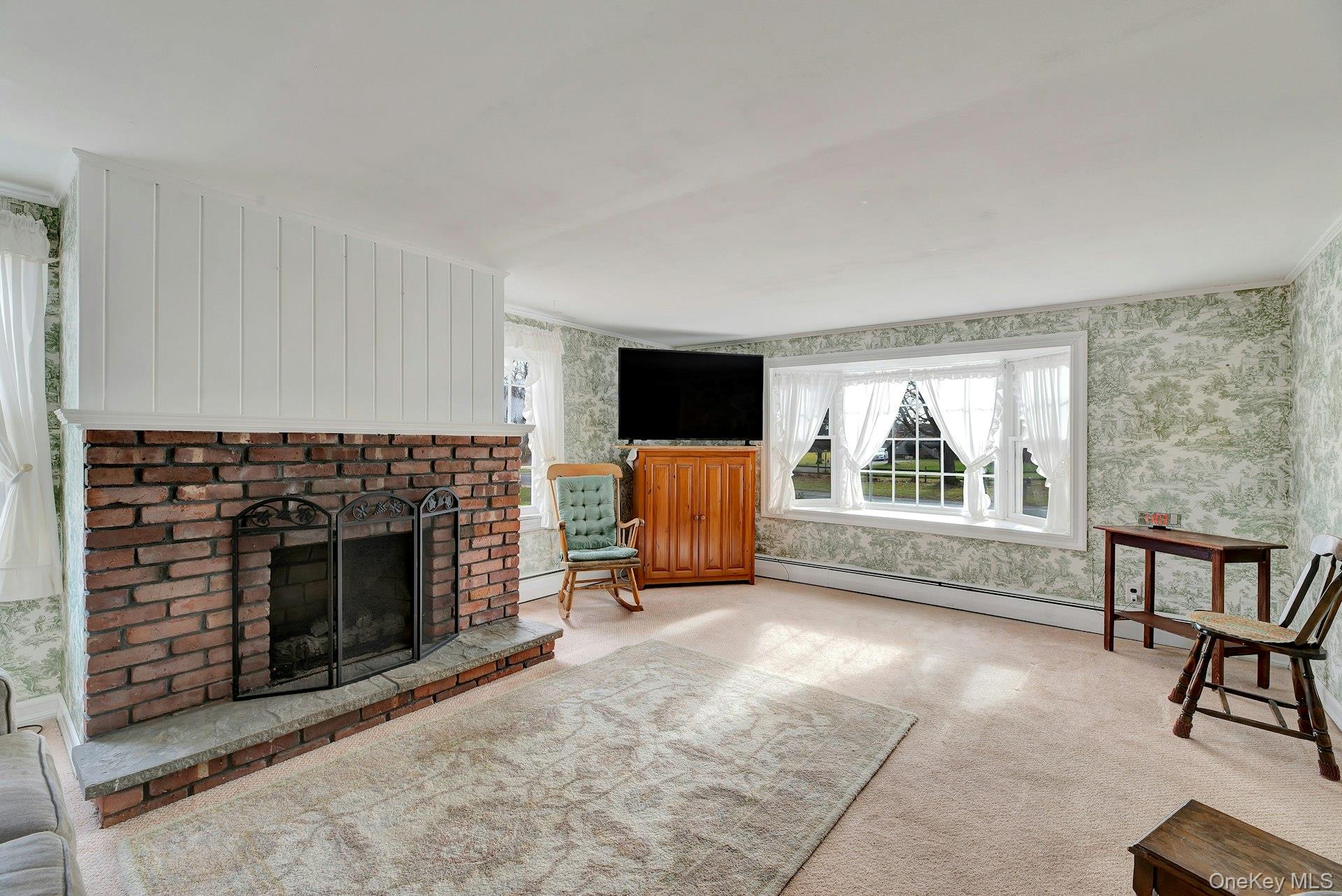 1760 Albertson Lane Greenport, NY 11944 - Photo 5 of 40 Unfurnished living room featuring a fireplace, wallpapered walls, a baseboard radiator, healthy amount of natural light, and carpet