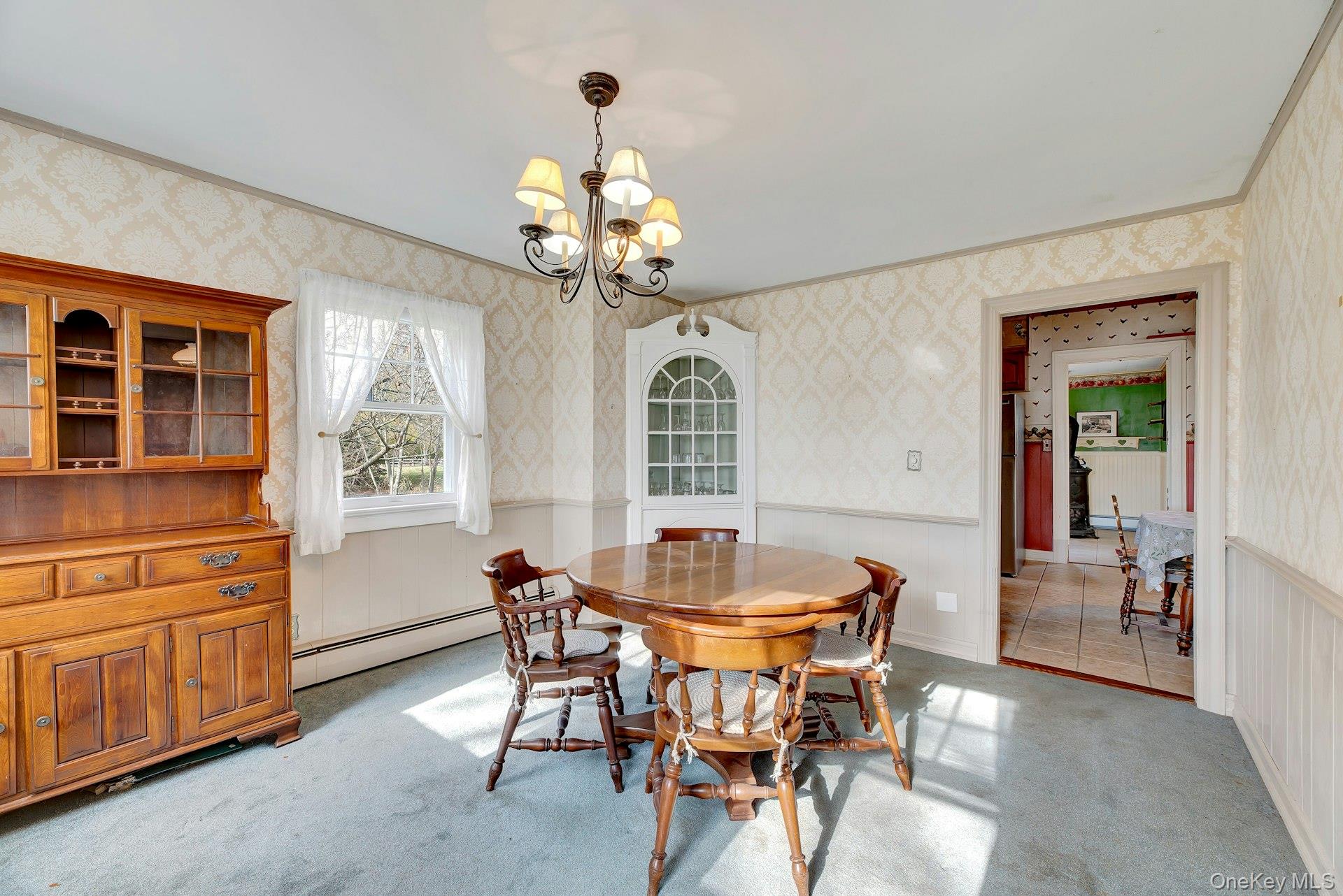 1760 Albertson Lane Greenport, NY 11944 - Photo 6 of 40 Dining space featuring wallpapered walls, wainscoting, light carpet, a chandelier, and a baseboard radiator