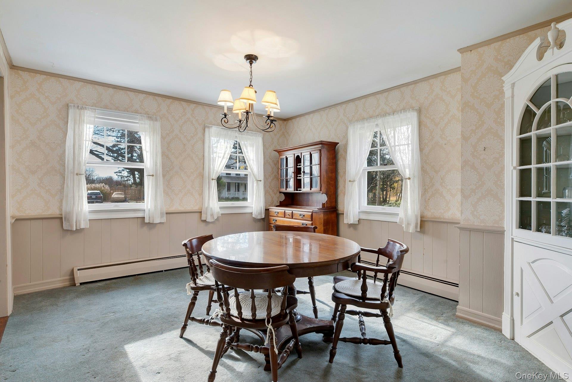 1760 Albertson Lane Greenport, NY 11944 - Photo 7 of 40 Dining area with wainscoting, wallpapered walls, baseboard heating, carpet floors, and a chandelier