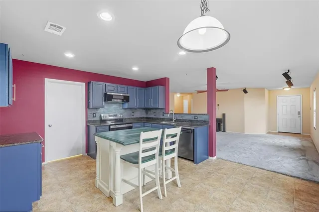 a kitchen with stainless steel appliances granite countertop a stove top oven a sink dishwasher and a refrigerator with wooden floor