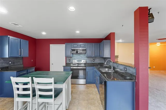 a kitchen with stainless steel appliances granite countertop a stove top oven a sink a dining table and chairs with wooden floor