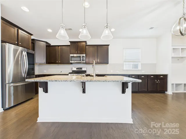 a kitchen with stainless steel appliances granite countertop a sink a stove a refrigerator a center island a stove and a sink