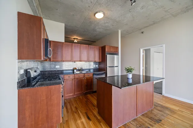 a kitchen with stainless steel appliances granite countertop a refrigerator a sink dishwasher a stove and a wooden cabinets