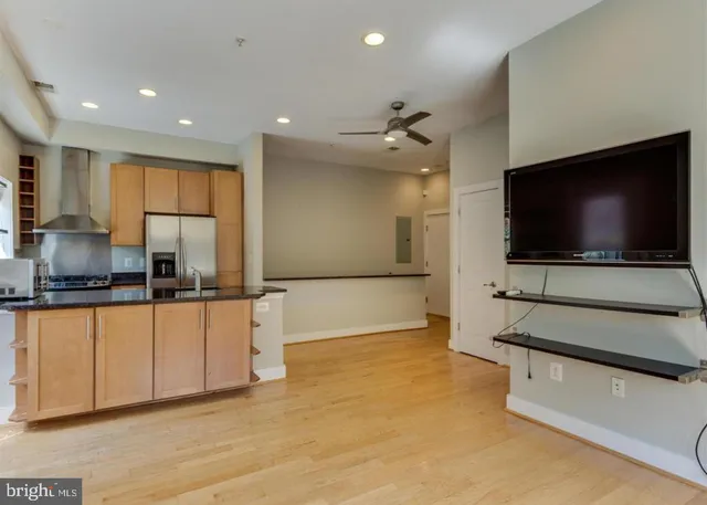 a living room with stainless steel appliances kitchen island granite countertop a sink and a stove top oven with wooden floor