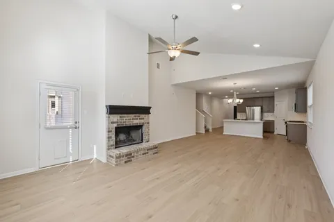 a view of a livingroom with a fireplace a ceiling fan a kitchen and chandelier