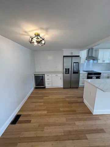 a kitchen with granite countertop a refrigerator a sink a stove and white cabinets with wooden floor