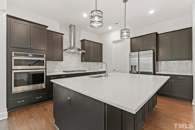 a kitchen with stainless steel appliances a stove a refrigerator and a sink with wooden floors