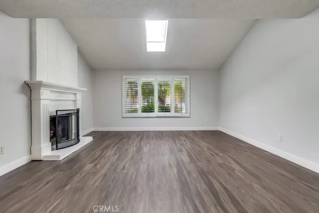 a view of an empty room with wooden floor fireplace and a window