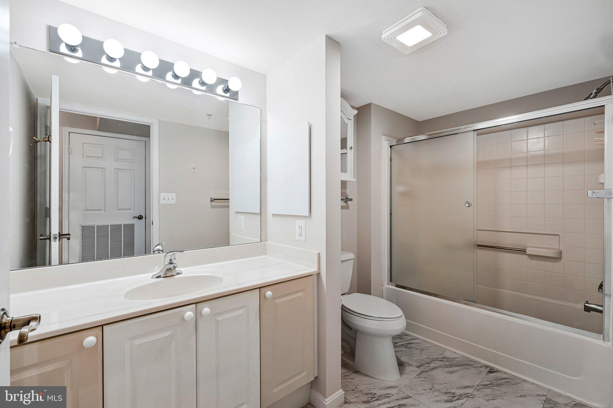 19385 Cypress Ridge Terrace, Unit 815 Leesburg, VA 20176 - Photo 20 of 35 a bathroom with a granite countertop sink a toilet a mirror and a glass door shower