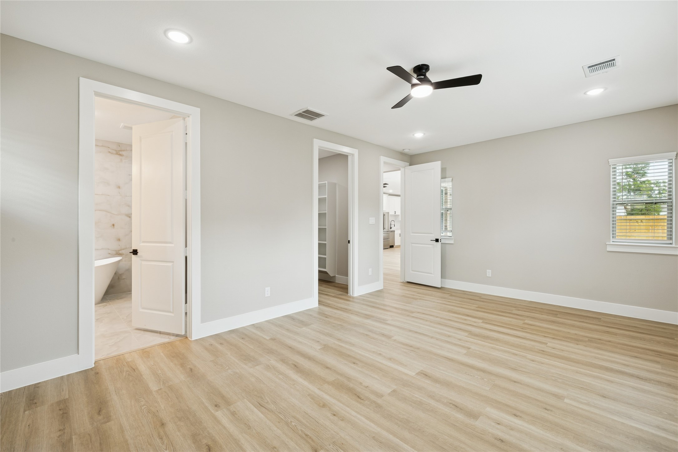 2522 Liguria Lane Spring, TX 77388 - Photo 12 of 35 This is a bright, spacious bedroom with light wood flooring and neutral walls. It features recessed lighting, a ceiling fan, and multiple doors leading to a bathroom and other areas. The room has ample natural light from the windows.