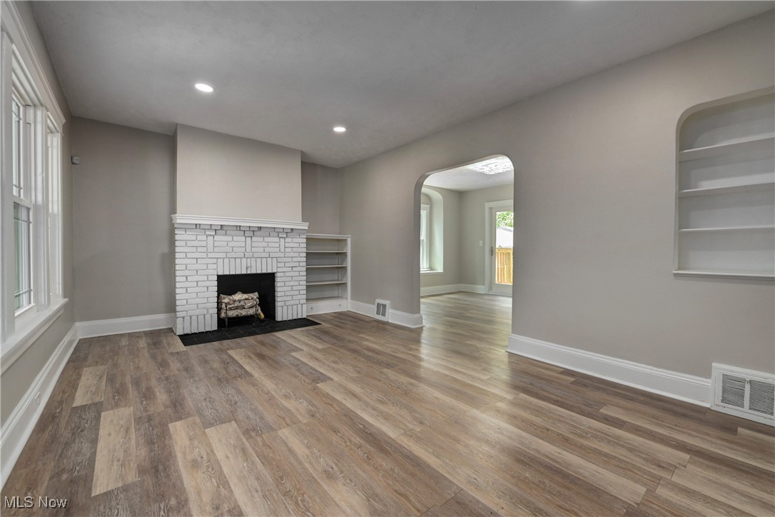 896 Selwyn Road Cleveland Heights, OH 44112 - Photo 5 of 23 Unfurnished living room with arched walkways, wood finished floors, recessed lighting, a brick fireplace, and built in shelves