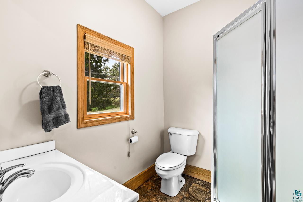 4800 Tower Road Moose Lake, MN 55767 - Photo 24 of 83 Bathroom featuring a single-sink vanity with chrome fixtures, a shower enclosure with frosted glass, a standard toilet, and a wood-framed window with natural light