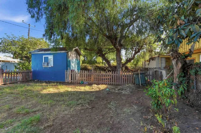 a view of a small yard in front of a house with large trees and wooden fence