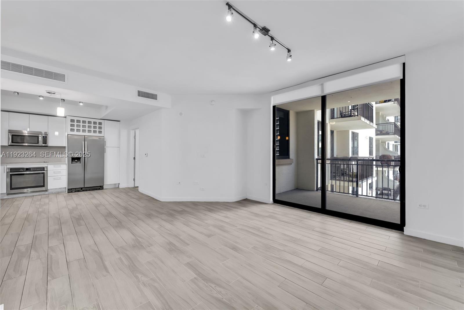 a view of an empty room with wooden floor and a kitchen