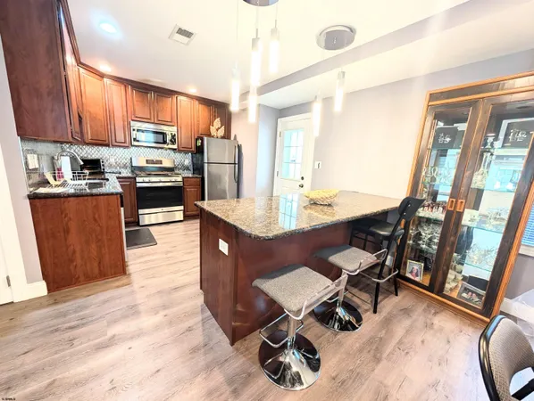 a kitchen with stainless steel appliances kitchen island granite countertop a stove a refrigerator a sink a dining table and chairs with wooden floor