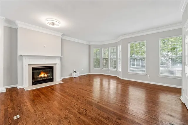 a view of an empty room with wooden floor fireplace and a window