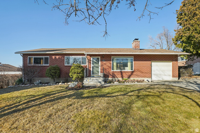Ranch-style house featuring brick siding, a front lawn, a chimney, and concrete driveway