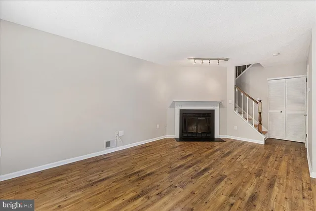 a view of an empty room with wooden floor fireplace and a window