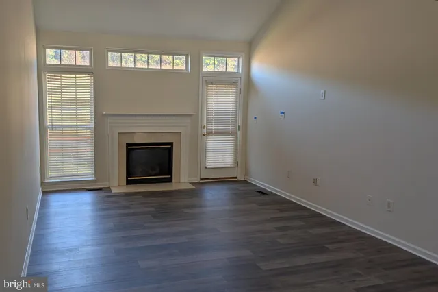 an empty room with wooden floor fireplace and windows
