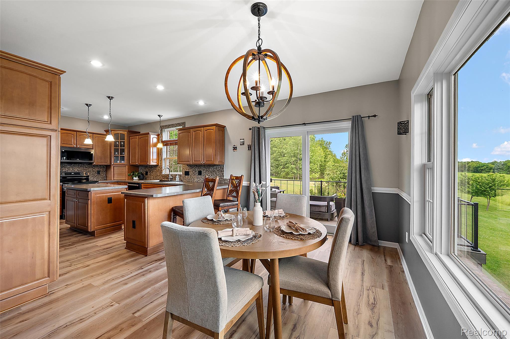 5035 Hidden Ridge Road Metamora, MI 48455 - Photo 16 of 65 Open-concept living space featuring wood-finish flooring, a contemporary chandelier, two-tone wall paneling, a full kitchen with wood cabinetry and dark countertops, and large windows with surrounding natural scenery