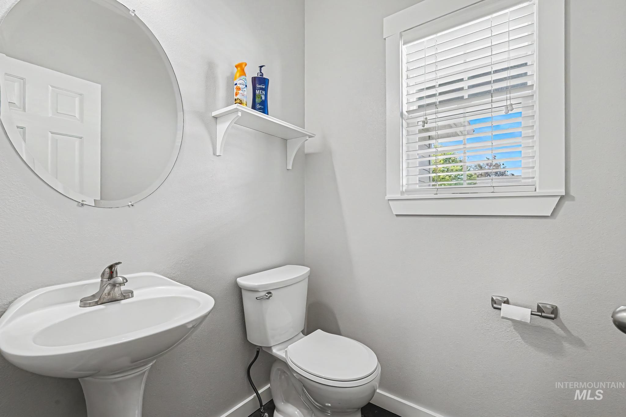 14421 West Stockwell Street Boise, ID 83713 - Photo 12 of 20 Pedestal sink with a chrome faucet, round wall-mounted mirror, and white window blinds