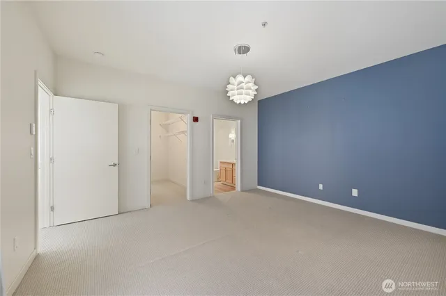 an empty room with chandelier fan and kitchen view