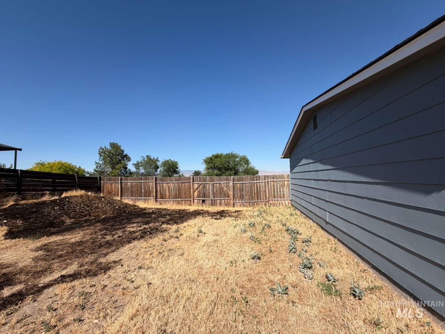 9951 West Fox Ridge Drive Boise, ID 83709 - Photo 4 of 13 Expansive backyard featuring a wood fence, mature trees, and a visible portion of the property's exterior with horizontal siding and a dark roofline