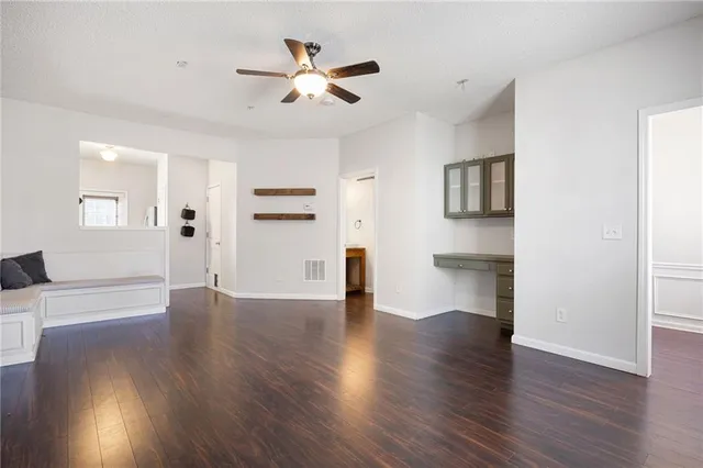 a view of an empty room with wooden floor and a ceiling fan