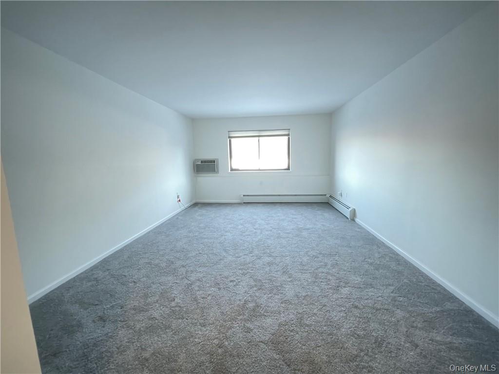27 Tanager Road, Unit 2702 Monroe, NY 10950 - Photo 13 of 17 Spacious room featuring gray carpeting, white walls, a window with natural light, a window-mounted air conditioning unit, and baseboard heating