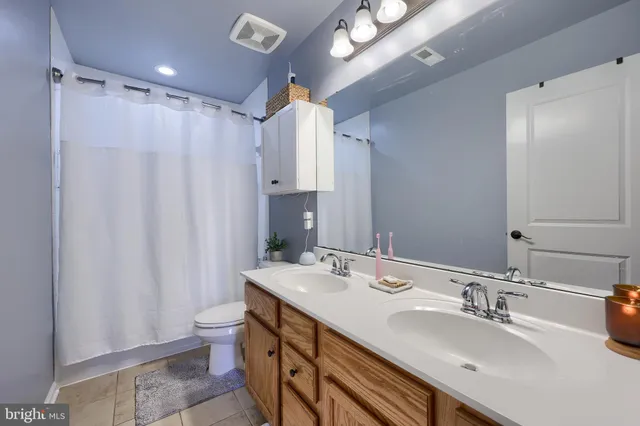 a bathroom with double vanity sink a toilet a mirror and shower curtain