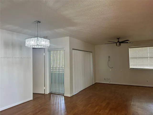 an empty room with wooden floor chandelier and windows
