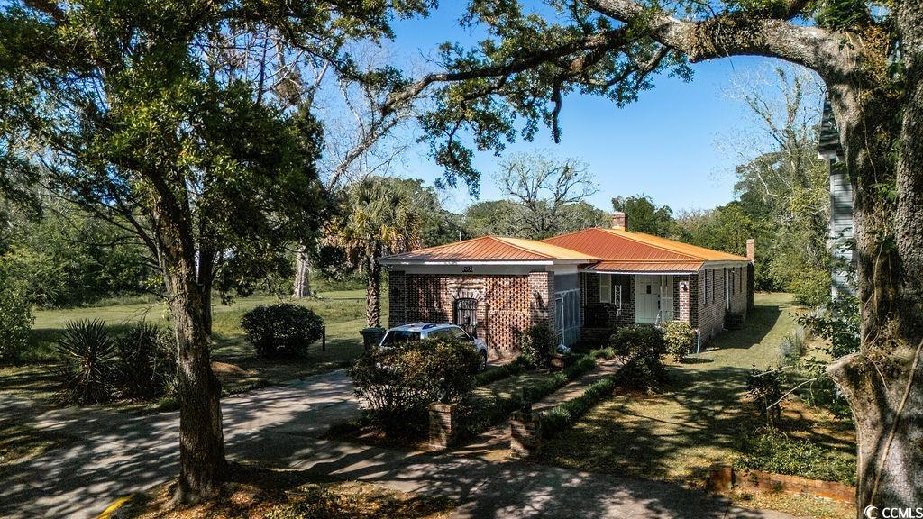 View of front of house featuring a chimney, a metal roof, brick siding, and a front yard