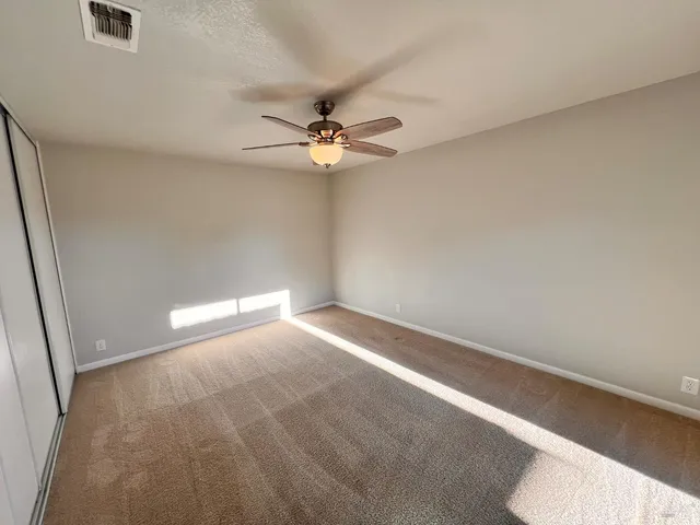 an empty room with a chandelier fan and windows