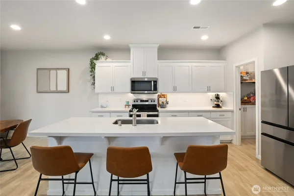 a kitchen with stainless steel appliances a dining table chairs refrigerator and microwave
