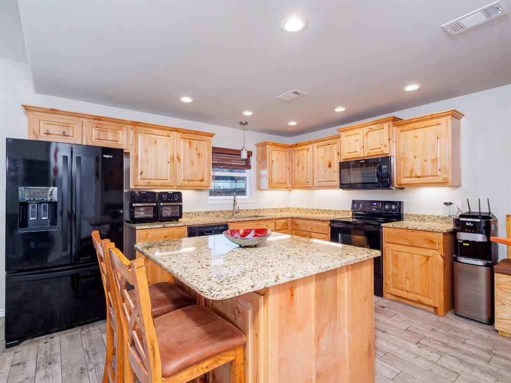 202 East Hall Court Early, TX 76802 - Photo 8 of 34 a kitchen with stainless steel appliances granite countertop a stove top oven a refrigerator a sink and a dining table with wooden floor