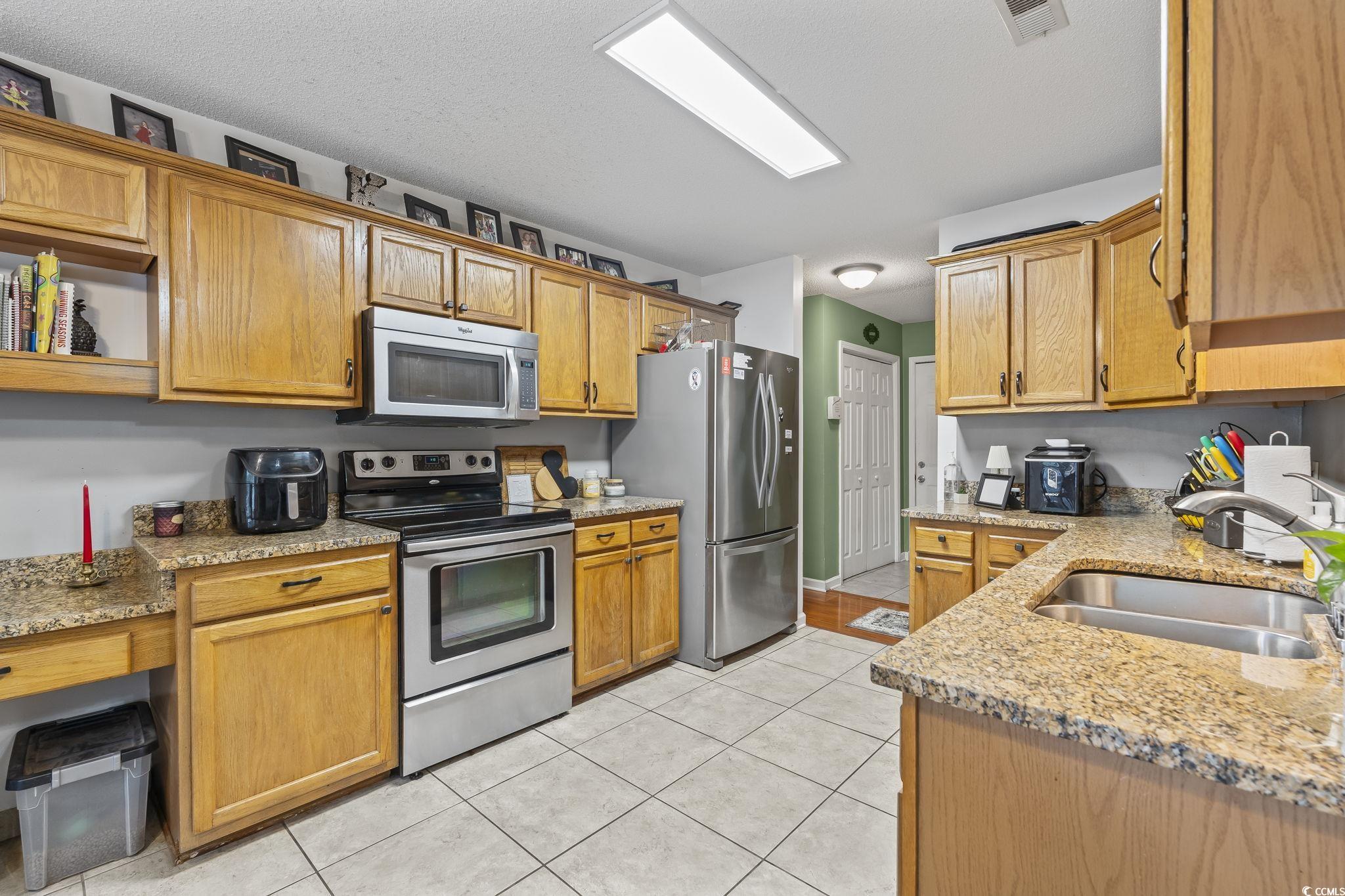 154 Hummingbird Court Myrtle Beach, SC 29579 - Photo 12 of 38 Kitchen with stainless steel appliances, light stone counters, light tile patterned floors, brown cabinetry, and open shelves