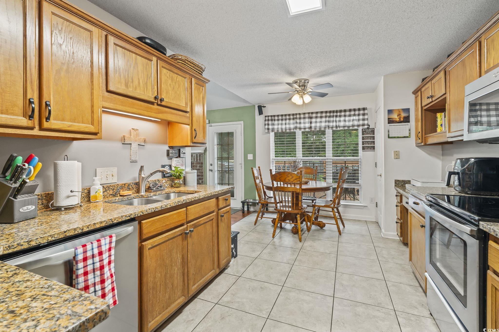 154 Hummingbird Court Myrtle Beach, SC 29579 - Photo 13 of 38 Kitchen with stainless steel appliances, light tile patterned flooring, light stone countertops, a textured ceiling, and brown cabinets