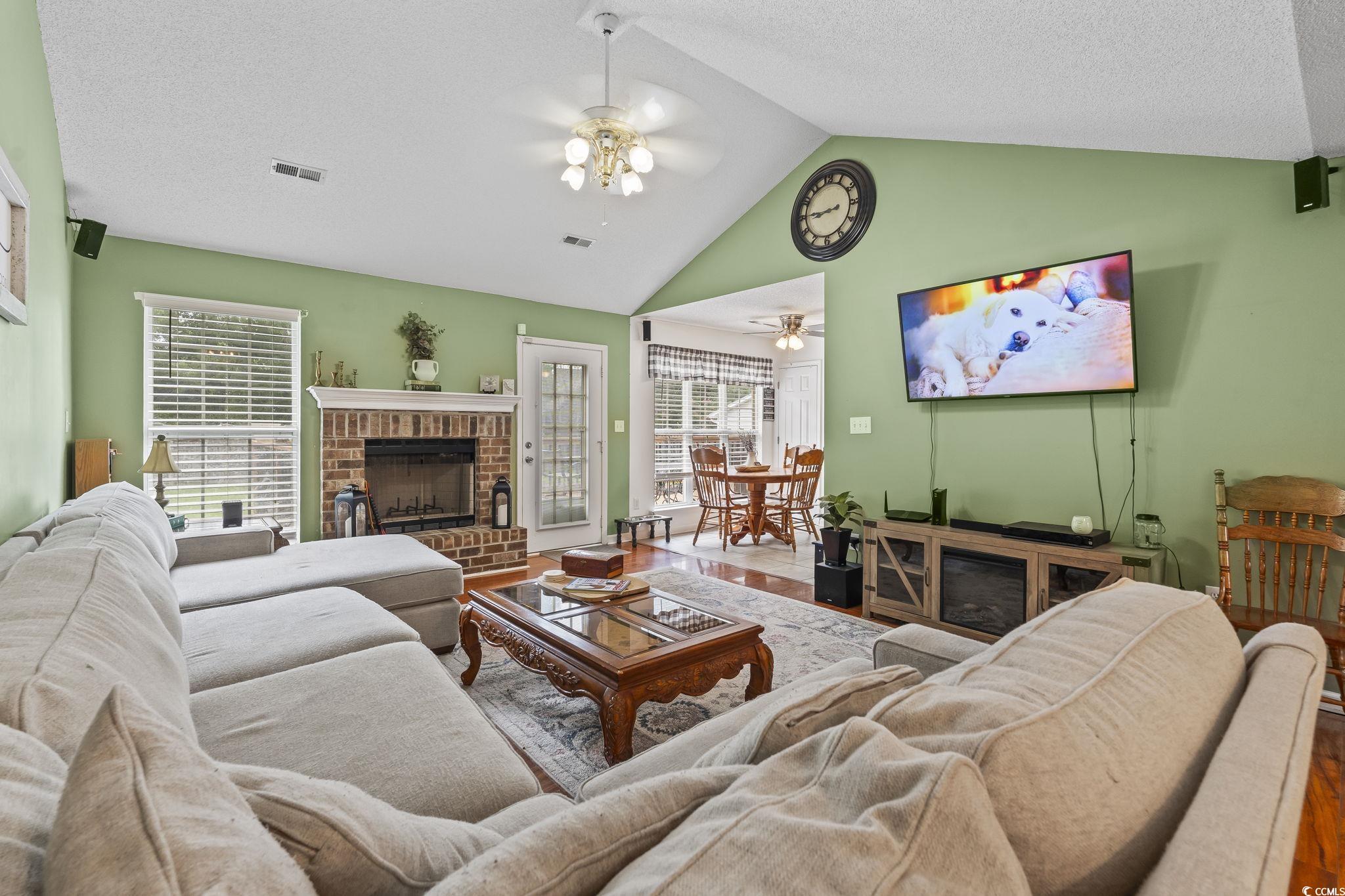 Living room featuring a fireplace, wood finished floors, ceiling fan, a textured ceiling, and high vaulted ceiling