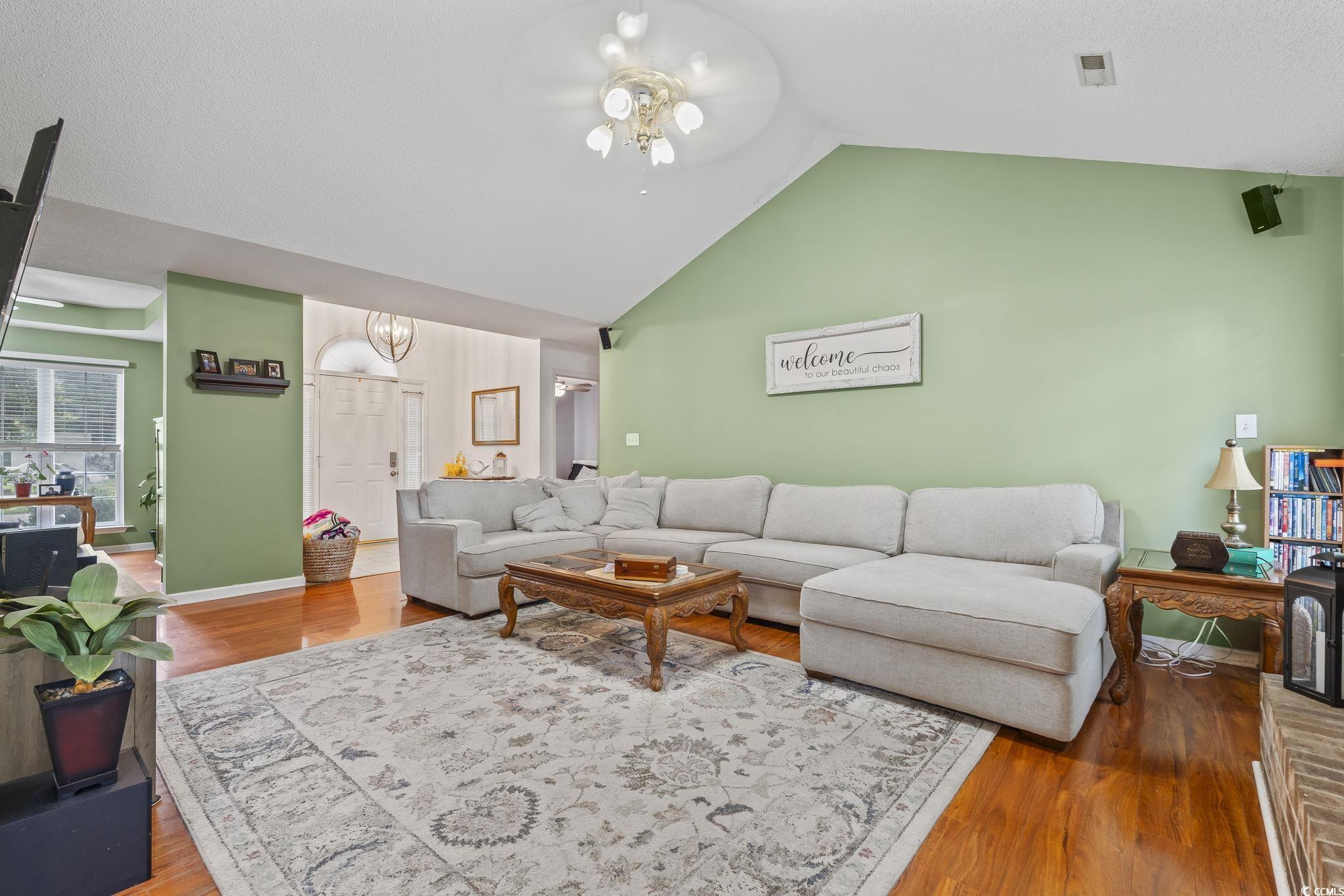 Living room with wood finished floors, high vaulted ceiling, and a ceiling fan