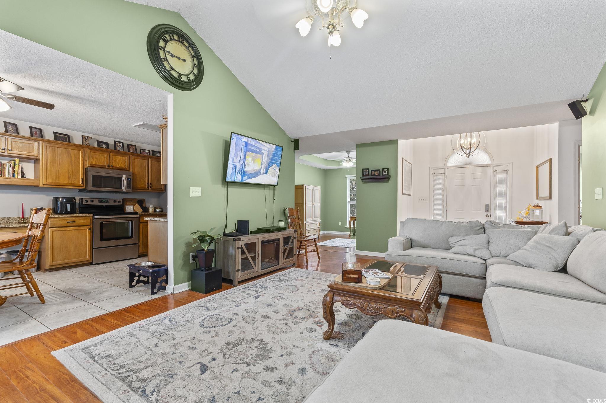 Living area with ceiling fan, light wood finished floors, vaulted ceiling, and a chandelier